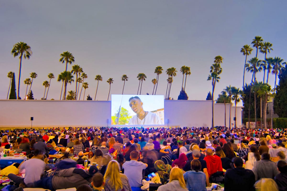 outdoor concert with musician on a large screen and palm trees in the background