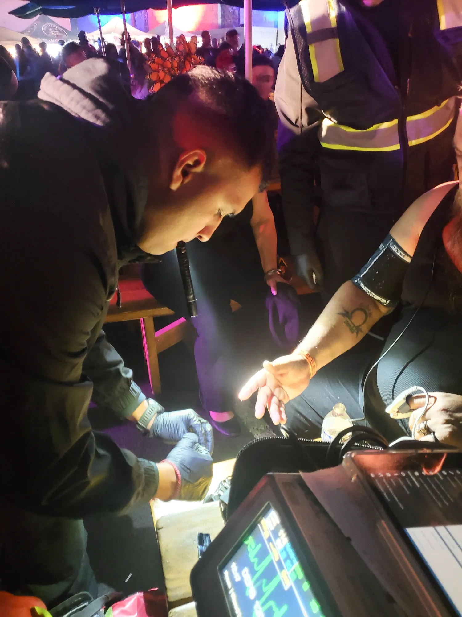 A paramedic wearing gloves and a flashlight in their mouth assisting a person at night.